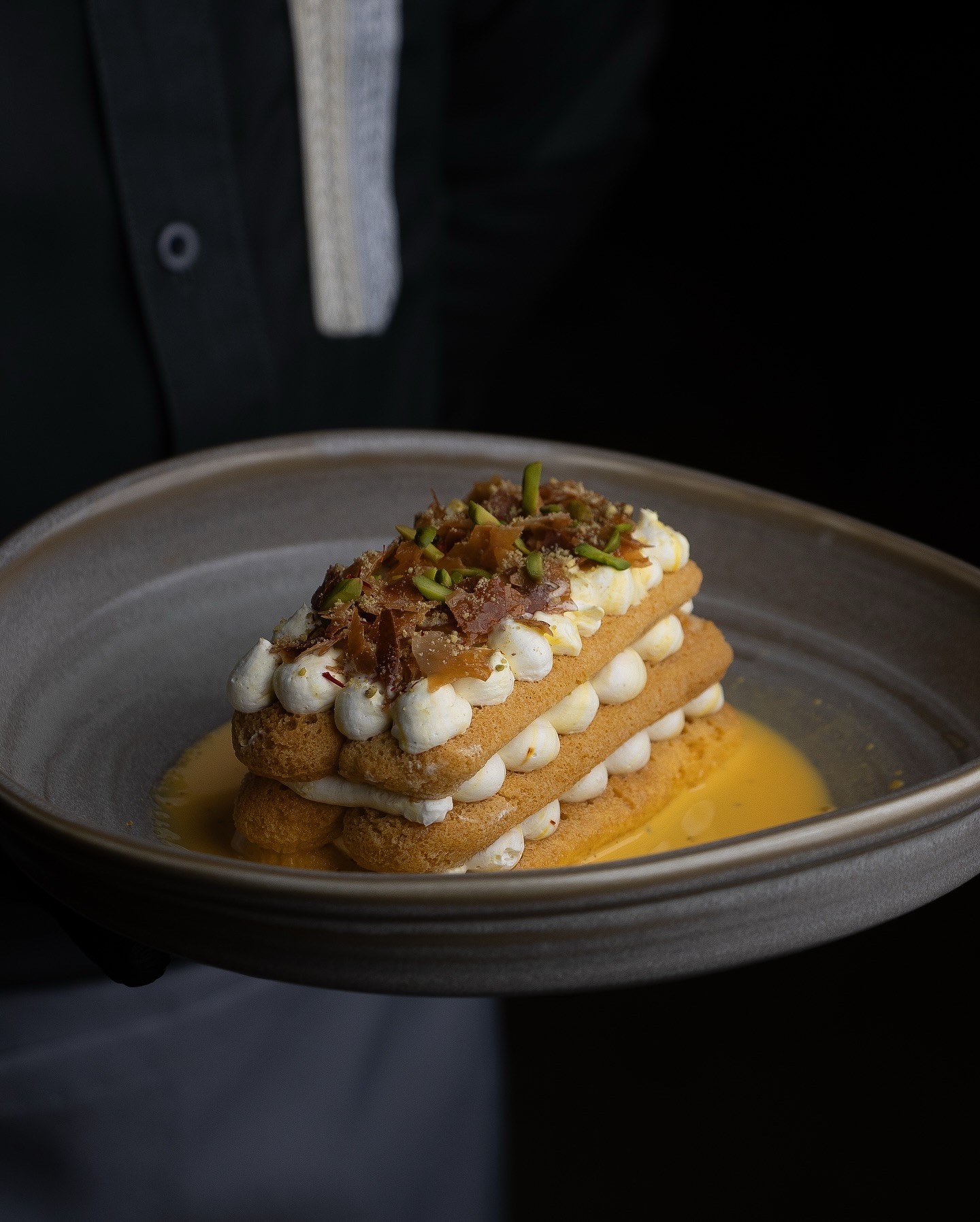 Wooden outdoor table set with multiple plates of food, including dips, salads, potatoes with cheese, and glasses of water, with hands reaching in to eat.