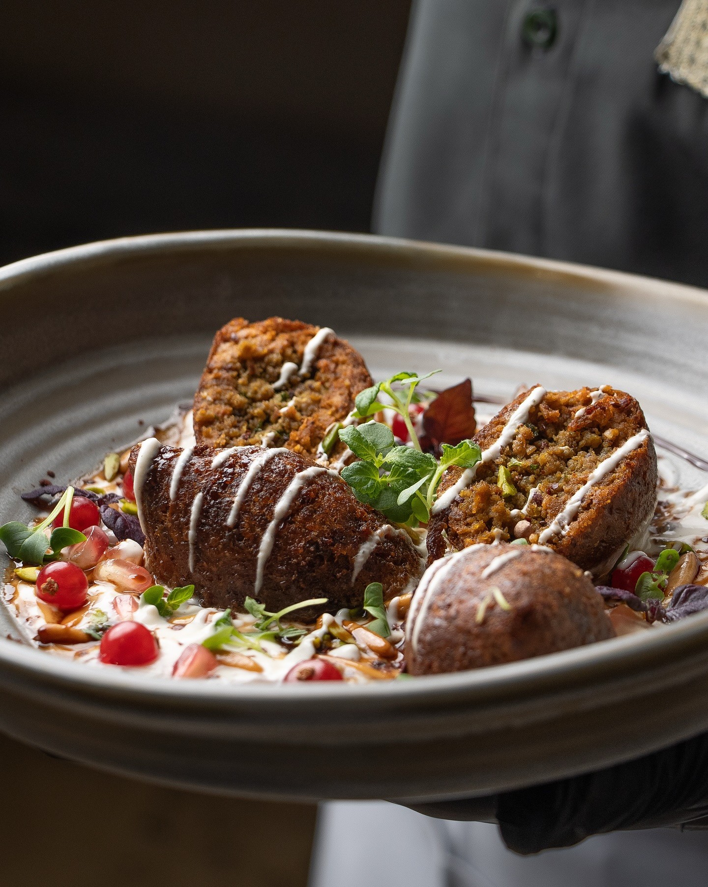 Restaurant interior with wooden tables and chairs lined against a textured wall, softly lit by round wall lamps.