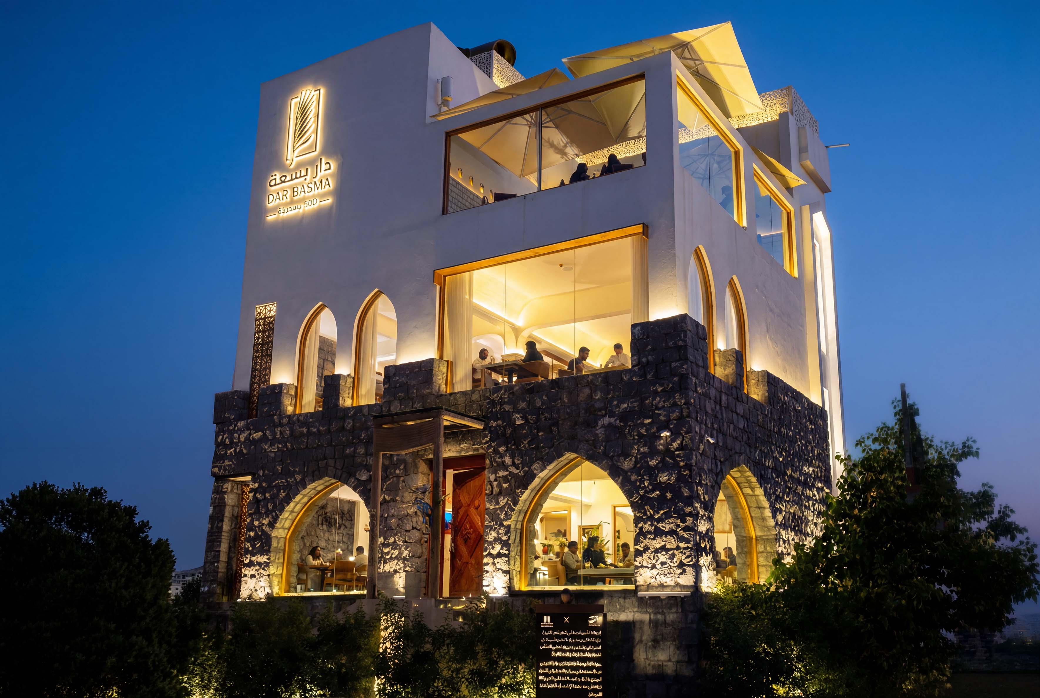 Plate with a seared salmon fillet topped with green herb garnish and sauce, served on a white dish placed on a dark green marble table beside a white candlestick.