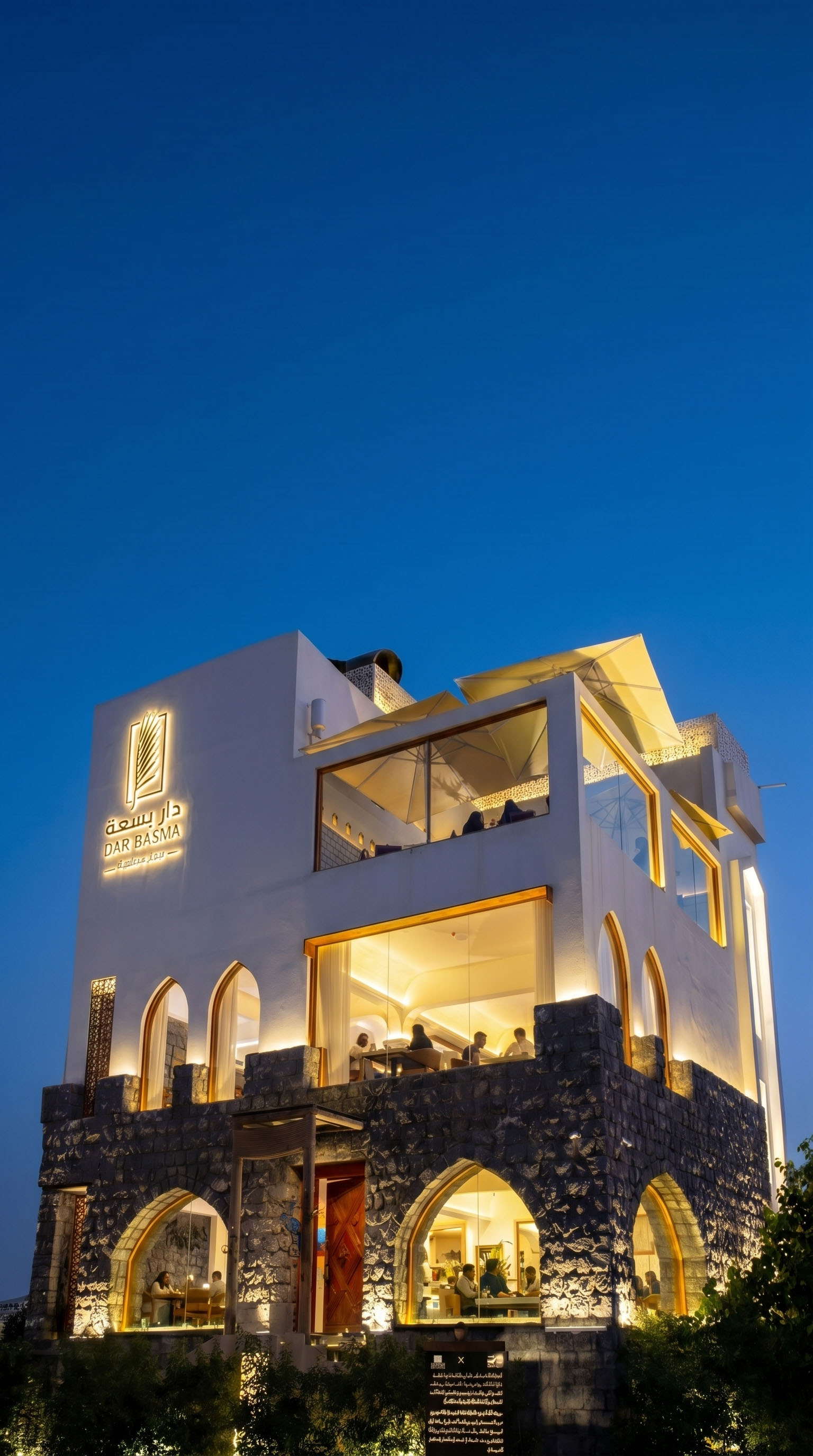 Plate with a seared salmon fillet topped with green herb garnish and sauce, served on a white dish placed on a dark green marble table beside a white candlestick.